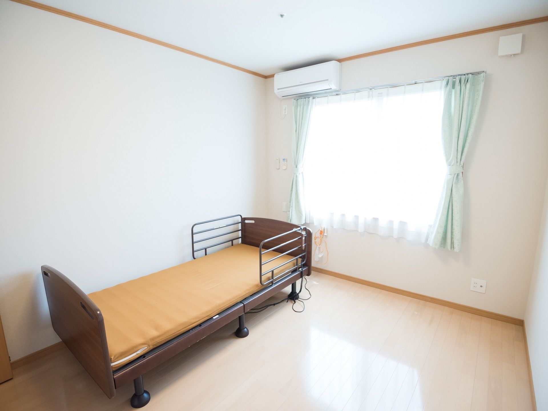 白を基調とした日当たりのよい居室である。カーテンやエアコン、介護用ベッド、ナースコールが完備されている。