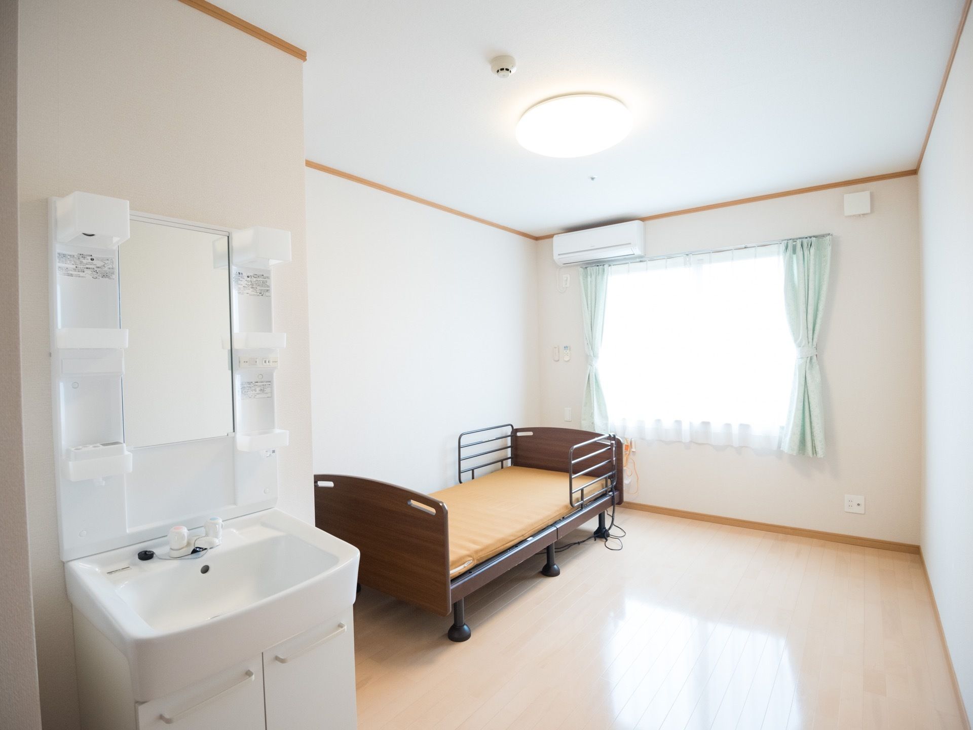 明るい居室にはベッドや洗面台が設置されている。エアコンがあるので、１年を通して快適に過ごすことができる。