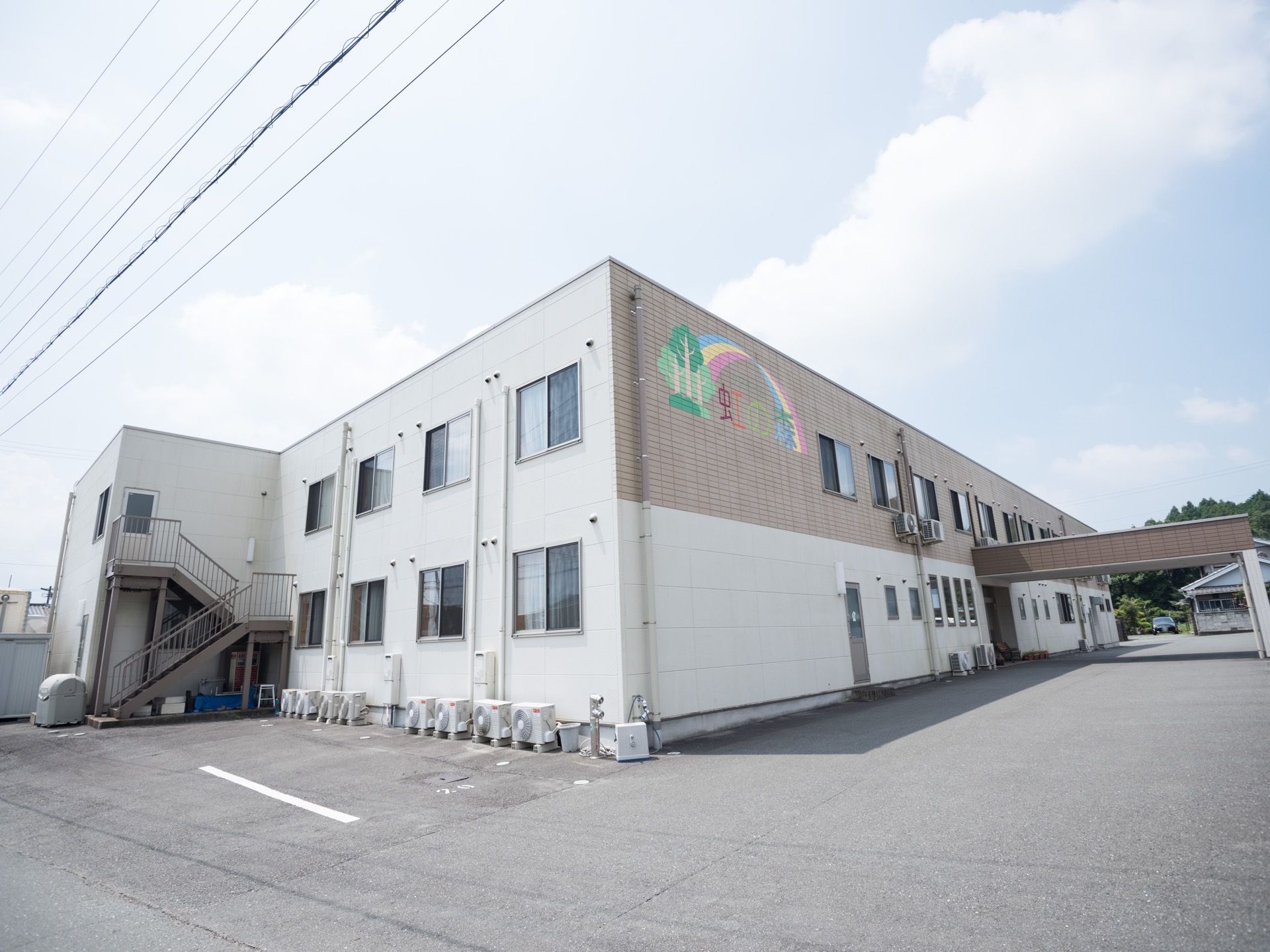 施設には外階段があり、２階建ての建物になっている。外壁には大きく施設名がペイントされている。玄関の前には屋根がある。