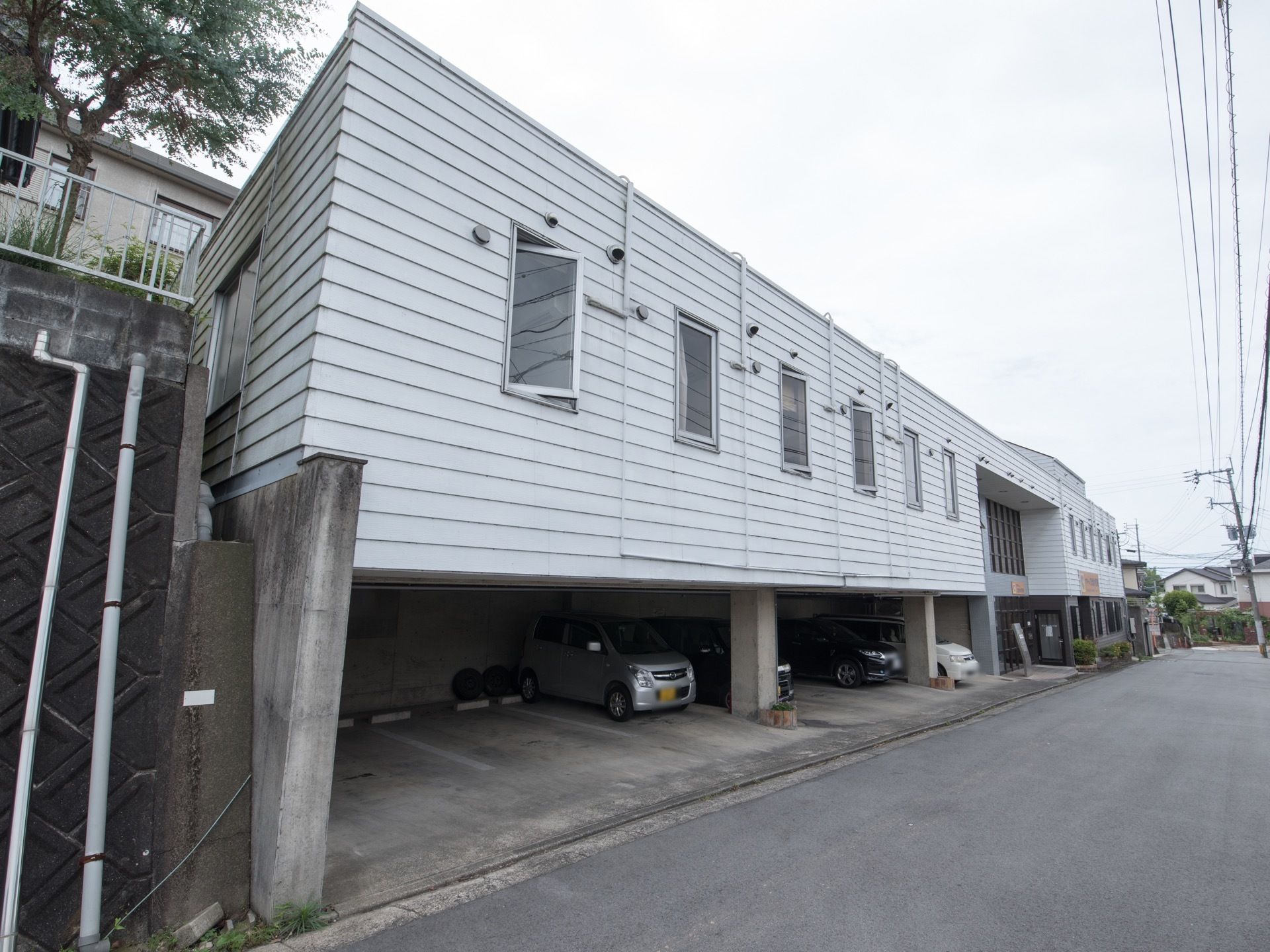 道路に面した場所に建つ施設である。１階が駐車場、２階が居室になっている。敷地のスペースを有効に使った設計である。