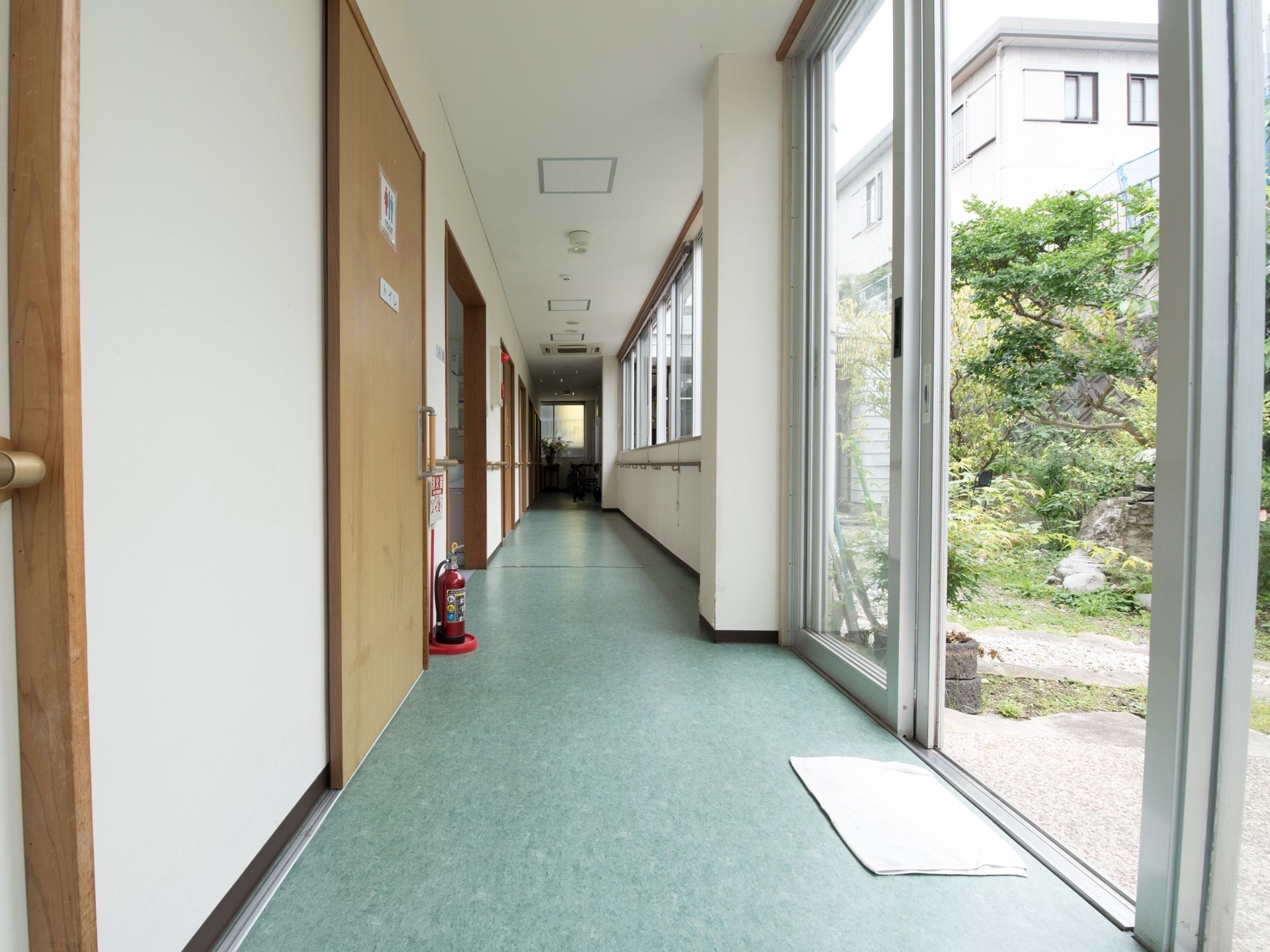 通路の床は薄い緑色で壁は白色である。トイレの扉には男性と女性のシルエットの紙が貼られていて、下側には消火器が置かれている。