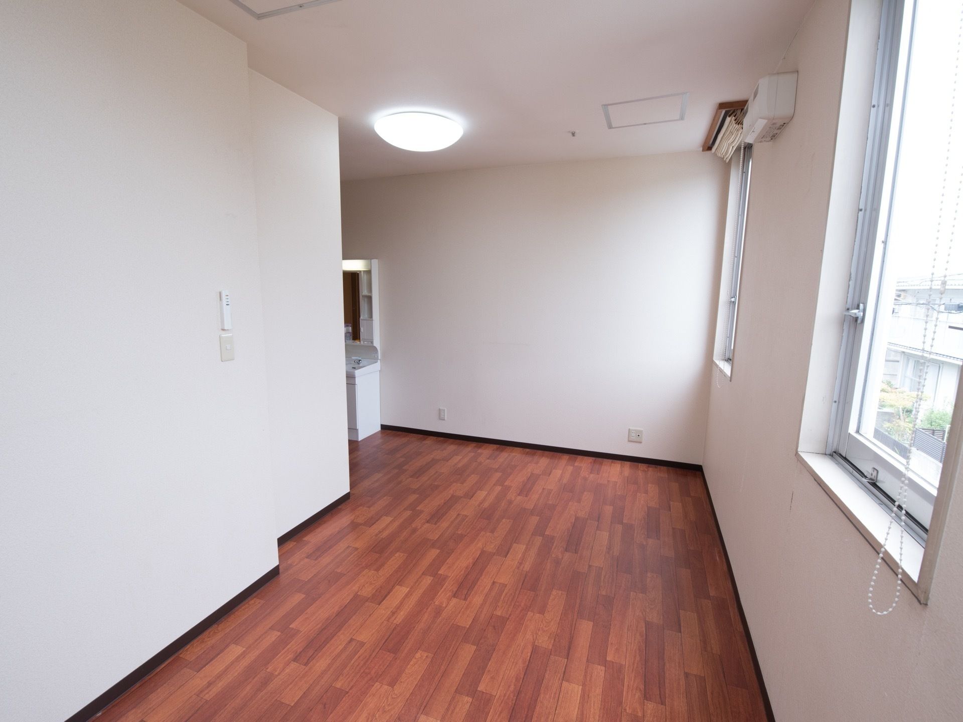 木目調の床、白色の壁と天井というデザインで、奥に洗面台が設置されている居室