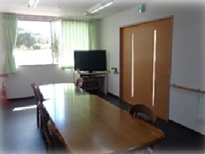 室内には窓があり、床には木製のテーブル、椅子、テレビが置かれている。壁には手すりが設置され、安全な設計になっている。