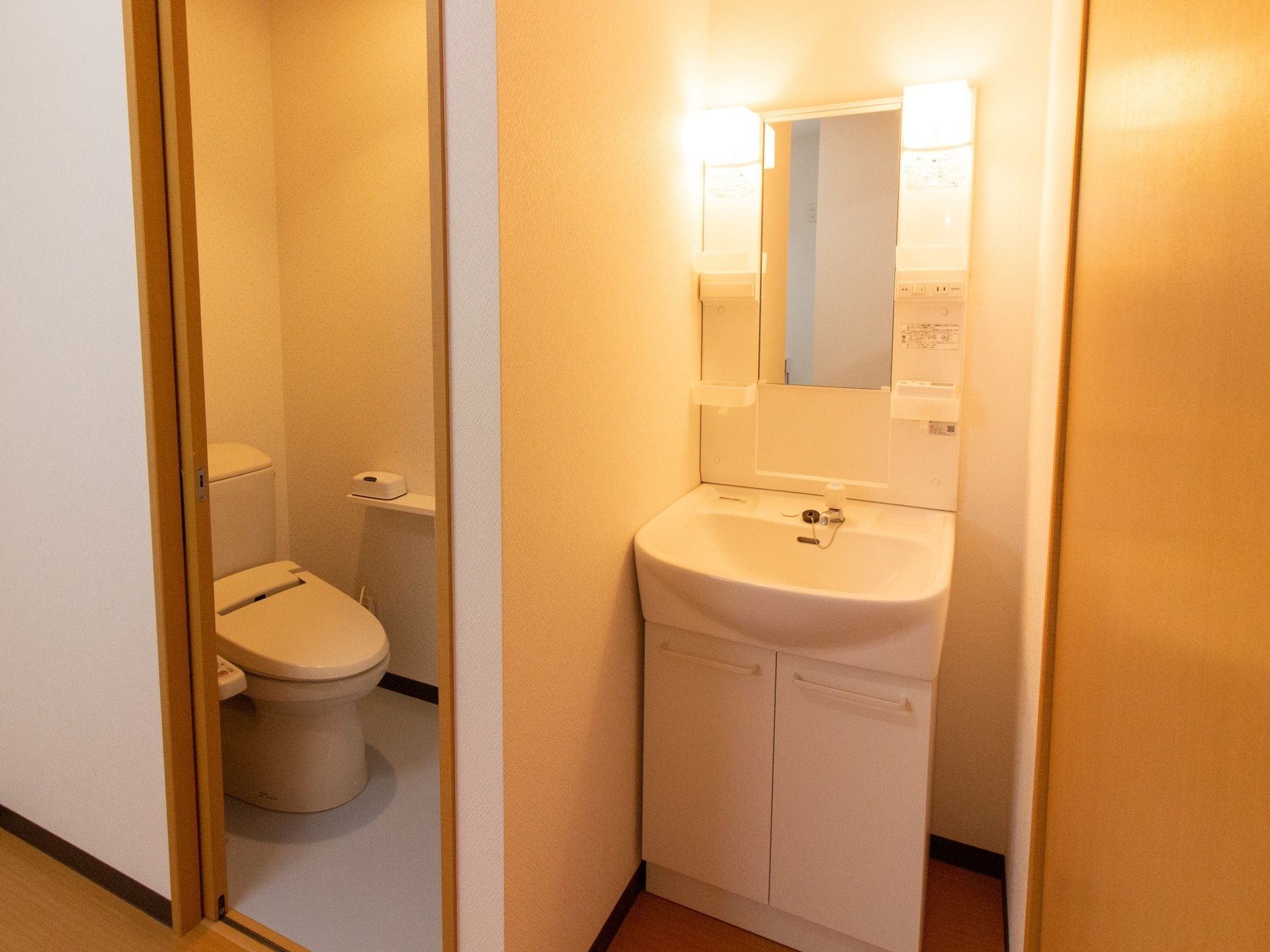 居室にある洗面台である。トイレの横の小さなスペースに設けられている。照明は温暖色でとても明るく、収納スペースも完備されている。