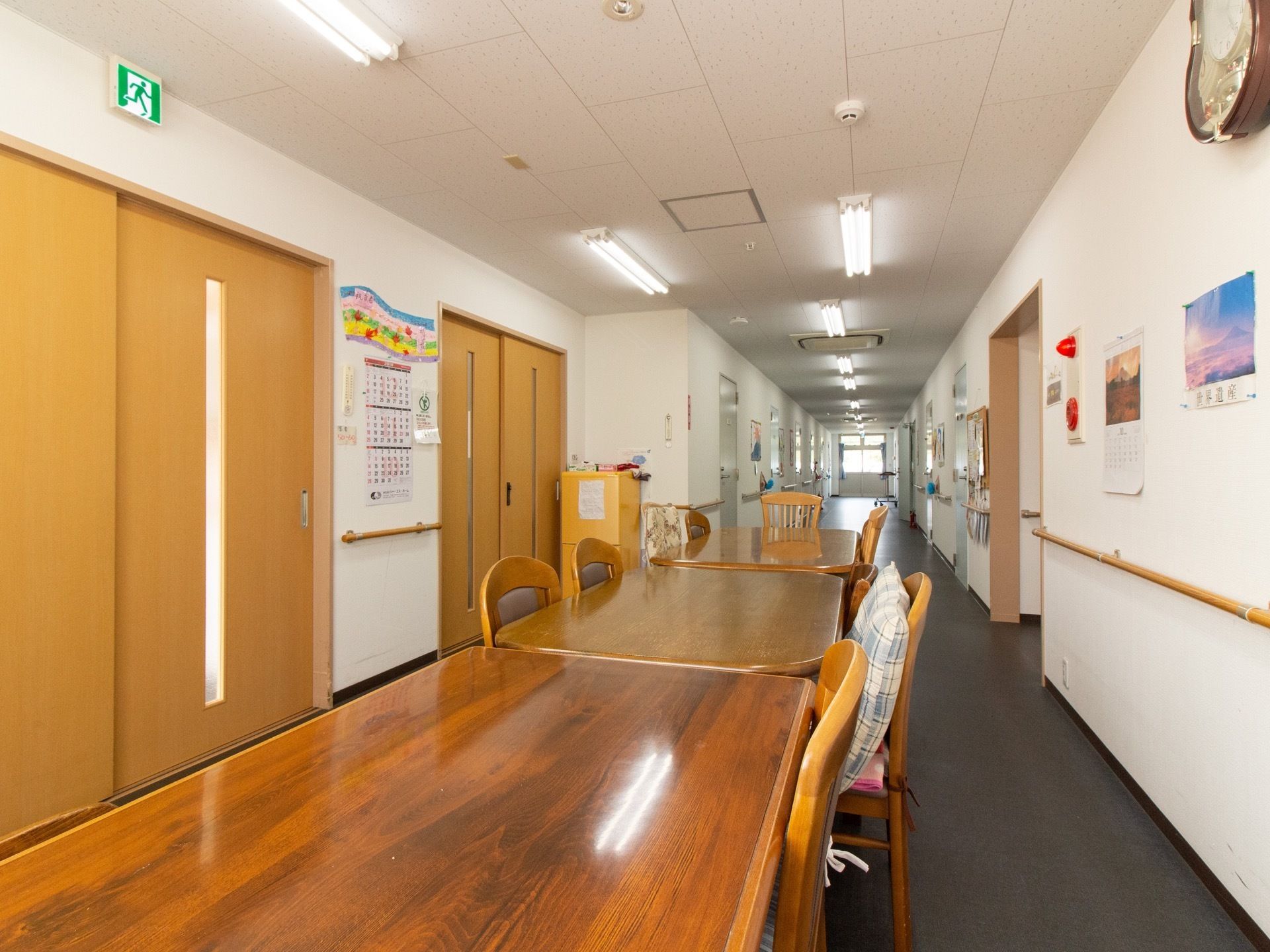 通路脇の広間にテーブルと椅子が並べられている。壁には時計やカレンダー、掲示板、ポスターが貼られている。