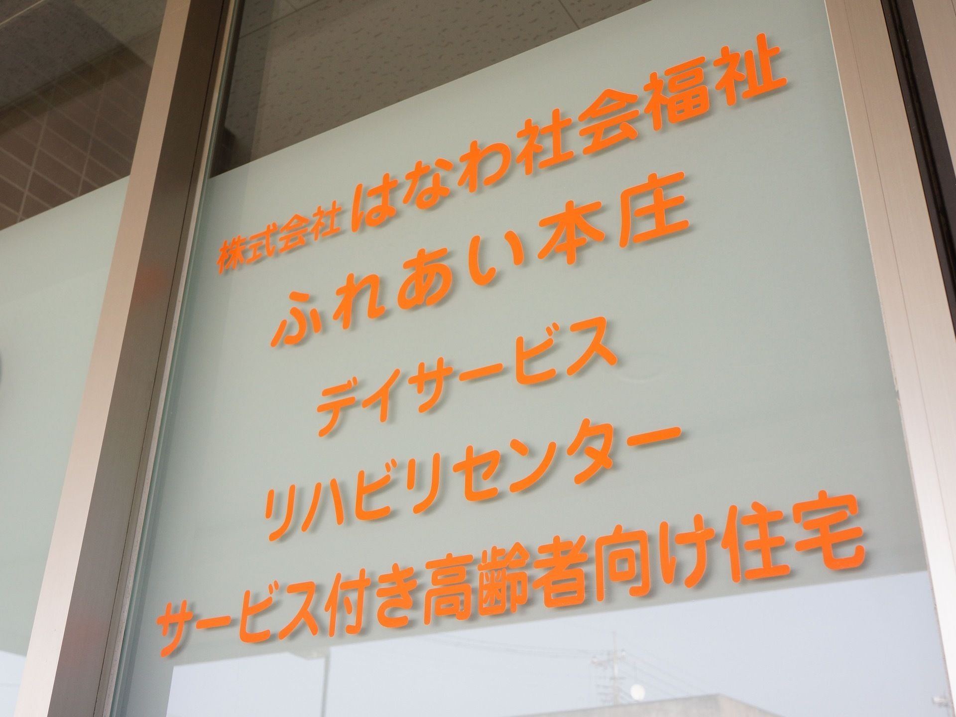 玄関は自動ドアが備わっている。透明のガラス部分にはオレンジ色の丸みを帯びた文字で、施設名が記されている。