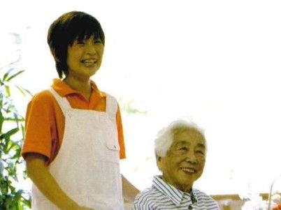 女性スタッフが車椅子をご利用の方の散歩に同行している。談笑しながらの気分転換に、ふたりとも笑顔が広がっている。