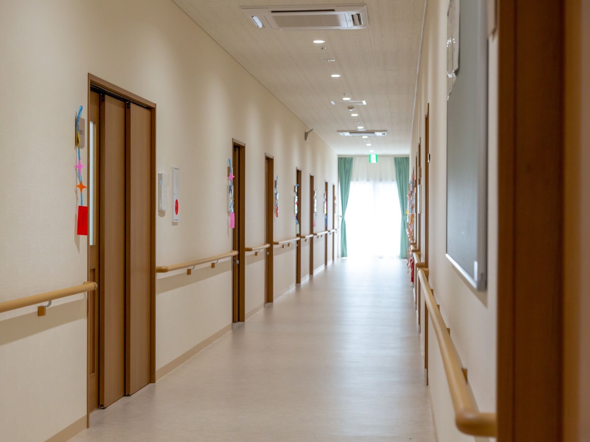 清潔に整えられすっきりと見通しの良い廊下は、白い壁に木目調の居室扉や設置されている手すりであたたかみがある。