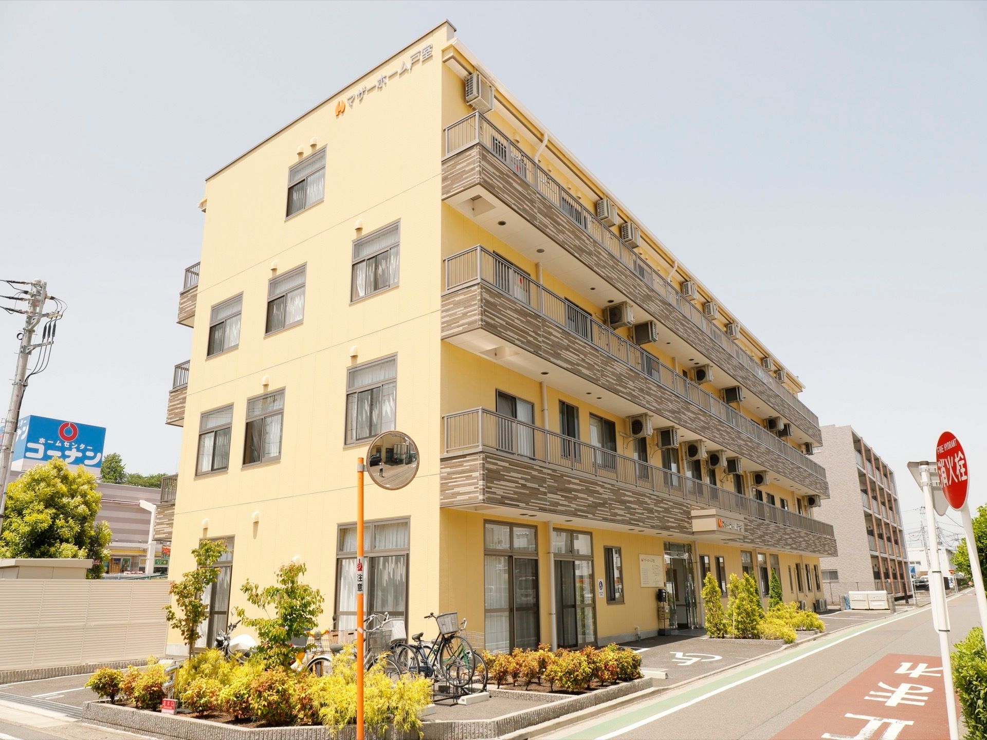 黄色い壁の、4階建ての建物である。２階以上の角界には、ベランダが設置されている。車椅子対応の駐車スペースがあるのが見える。
