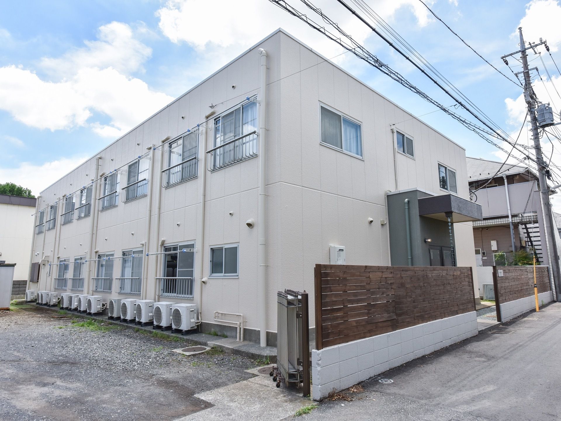 建物は全面が白く塗られ、玄関部はグレーになっている。道路と敷地の仕切の塀は、木製の板が貼られている。