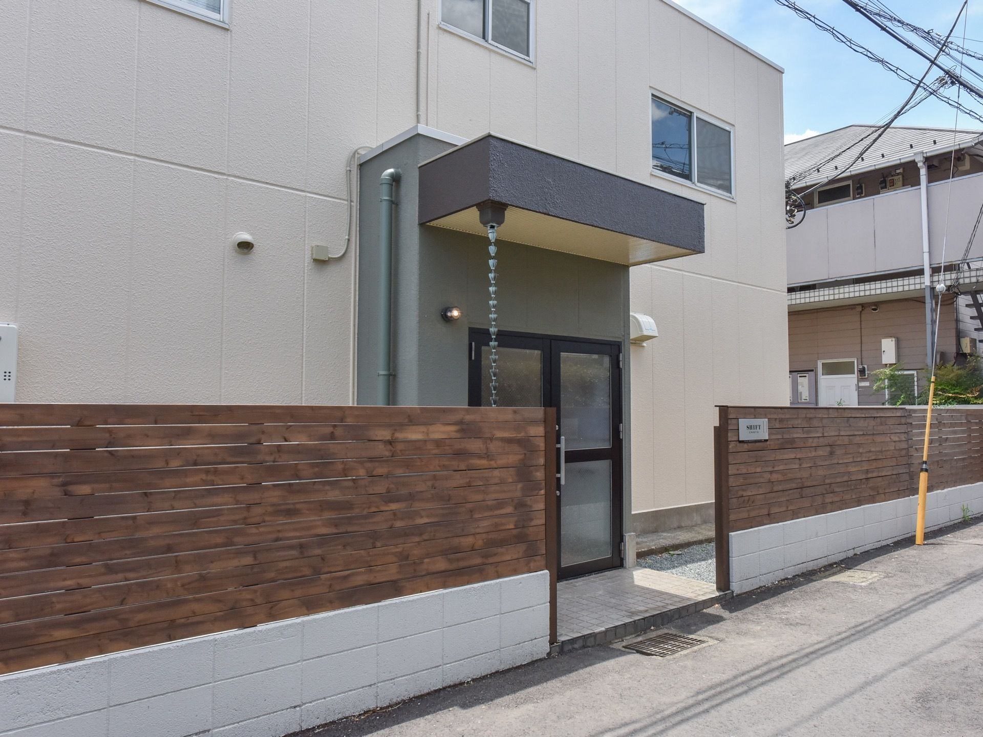 観音開きで開く玄関前には屋根がせり出している。木製のフェンスに施設名の書かれた看板が取り付けられている。