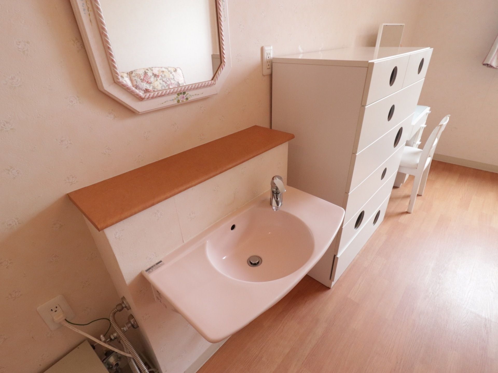 居室内に完備されている洗面台と鏡である。やさしい配色の洗面ボウルにセンサー付き水栓が設置されている。