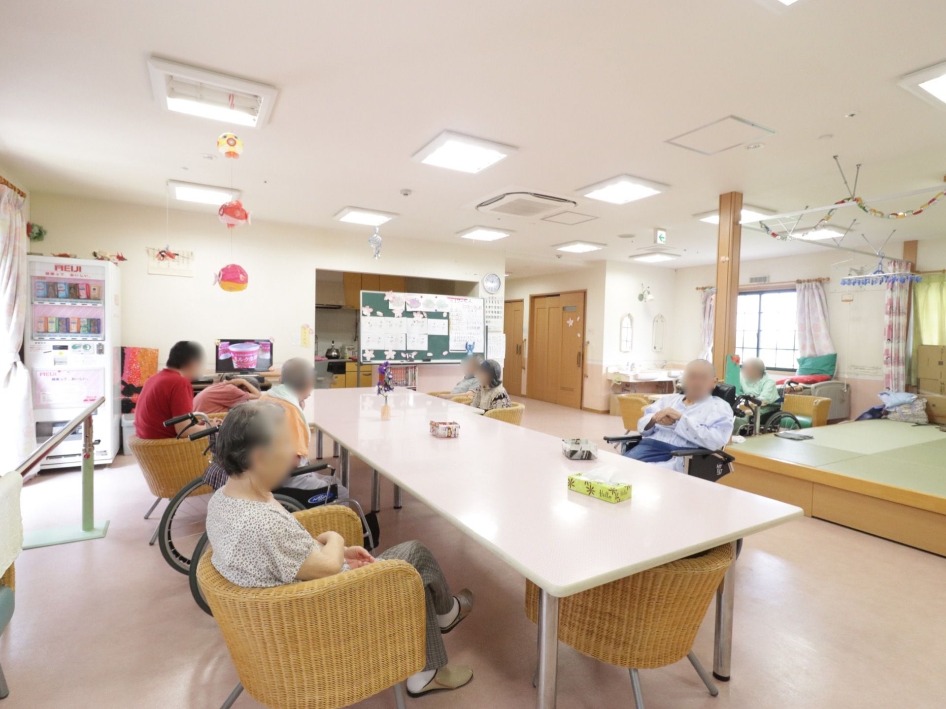 部屋の中央に長テーブルが置いてあり、入居者様が囲んで腰を掛けている。小上がりになった畳スペースがある。