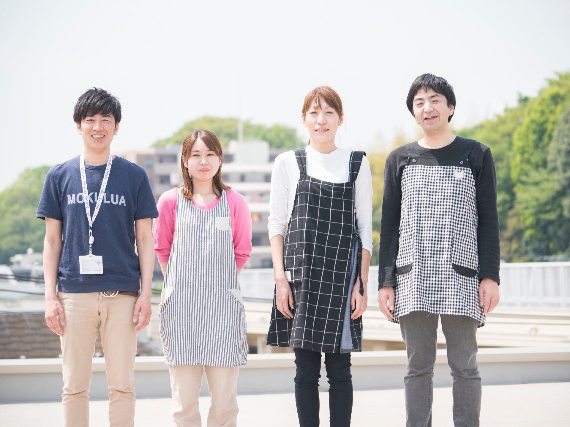 エプロンや名札を首から下げたスタッフが４人優しく微笑んでいる様子
