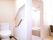白で統一された清潔感のあるトイレがあり、隣には浴室が設けられている。トイレの壁には赤い手すりが取り付けられている。