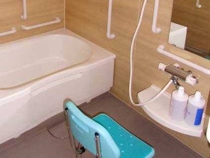 木のぬくもりが感じられる浴室である。壁には手すりが多数設置されており、洗い場にはシャワーチェアが置かれている。