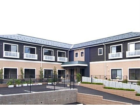 施設の建物は２階建てで、玄関には屋根が設けられている。入口までスロープとつながっている。また玄関前には駐車場がある。
