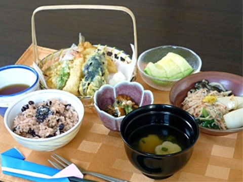 膳の上には敷物が敷かれ、赤飯、天ぷらなどの副菜、漬け物、味噌汁のほかにフルーツもあり、箸とフォークが置かれている。
