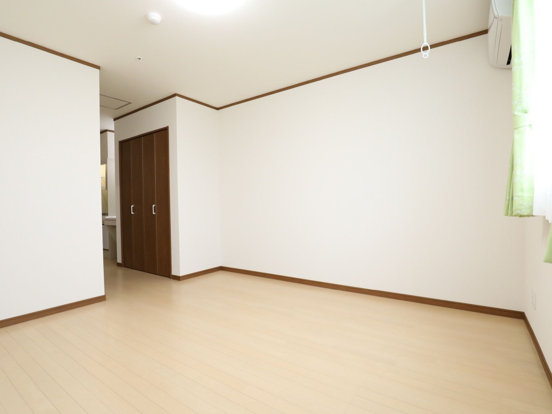 白い壁の居室ででこぼこのない長方形の部屋である。洗面台の横に折り戸式の収納スペースが用意されている。