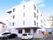 白い4階建ての建物。1階に自動販売機が設置してある。玄関近くには、入居者様および来訪者様用の駐車場がある。