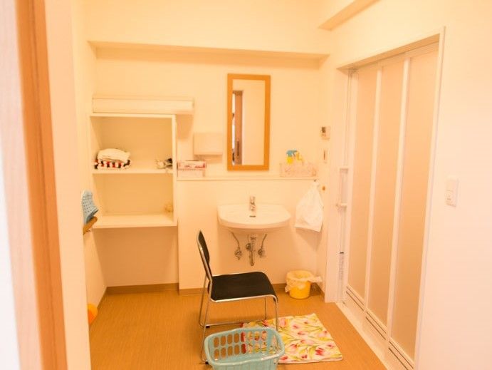 あたたかい色合いの広い脱衣所。三段の大きな棚には、入浴に必要なものを置くことができる。床は段差がないため安全である。