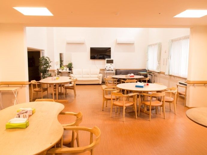 角のない机、イス、ソファがあるダイニング。壁掛けのテレビと娯楽機器もあるため、入居様同士が楽しめる空間となっている。