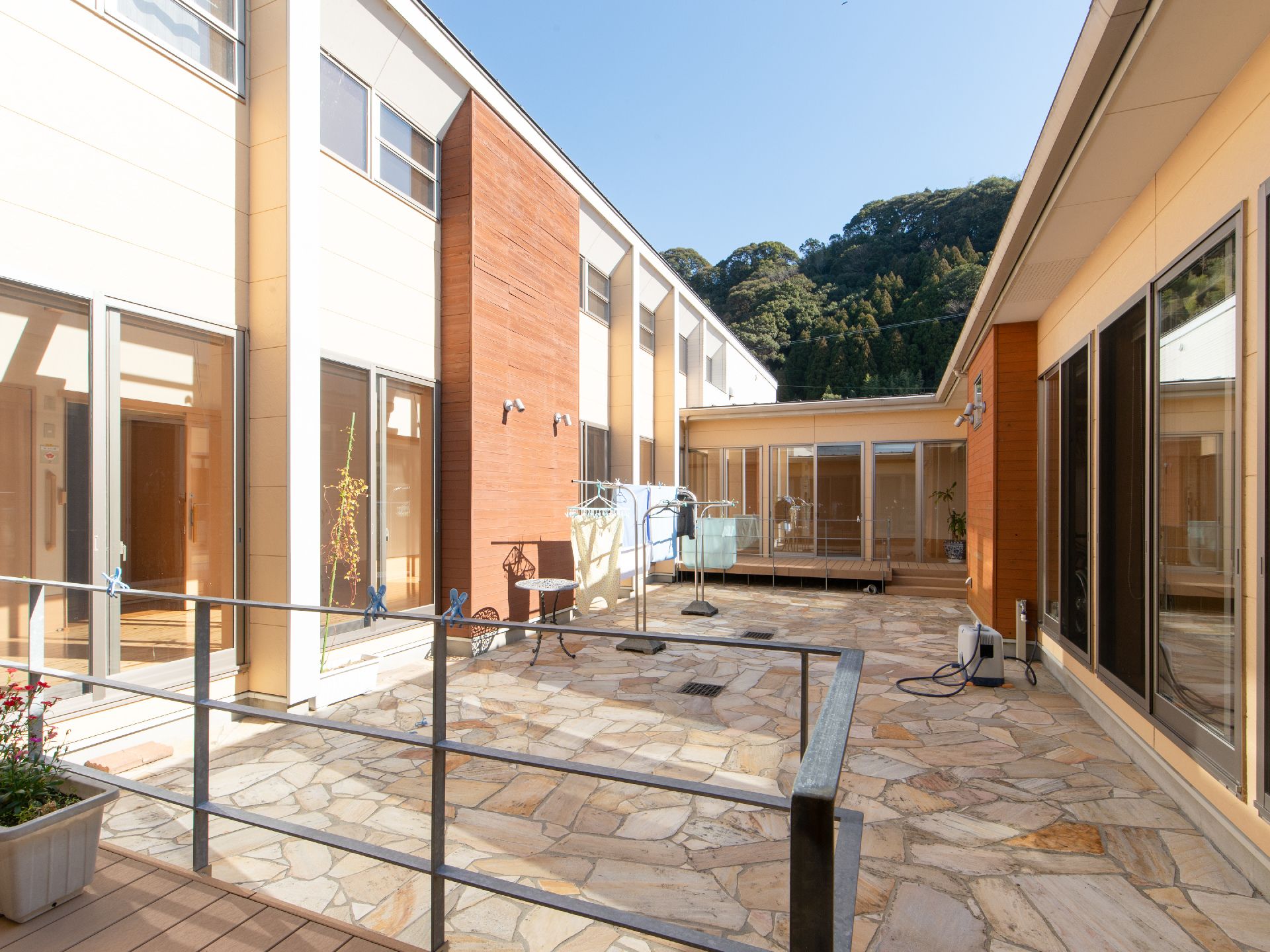 ヨーロッパの石畳調の中庭を廻るかたちで、廊下が連続している施設。建物の向こう側に、緑の茂みが見える。