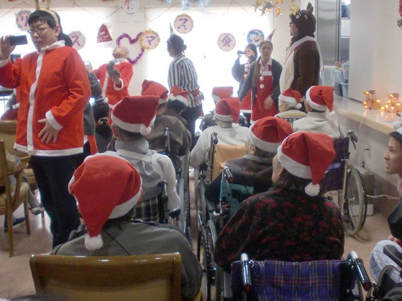 サンタクロースやトナカイの扮装をしてクリスマスイベントを楽しむ高齢者と介護スタッフ。