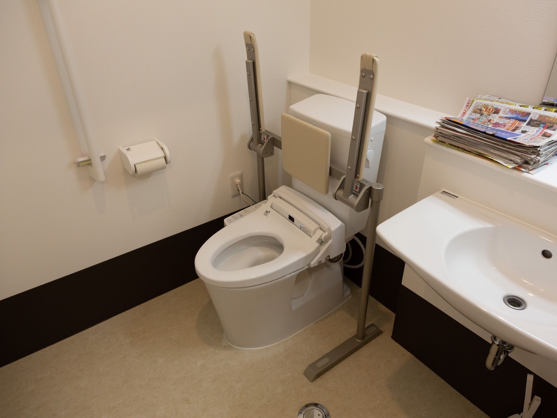 洗浄機付きのトイレには背もたれも取りつけられている。可動式の肘掛けのほか、壁にも手すりが設置されている。