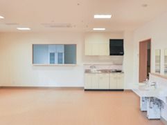 白い壁に囲まれた清潔感のある部屋に、コンロ付きのミニキッチンが設置されており、手前には洗面台が置かれている。