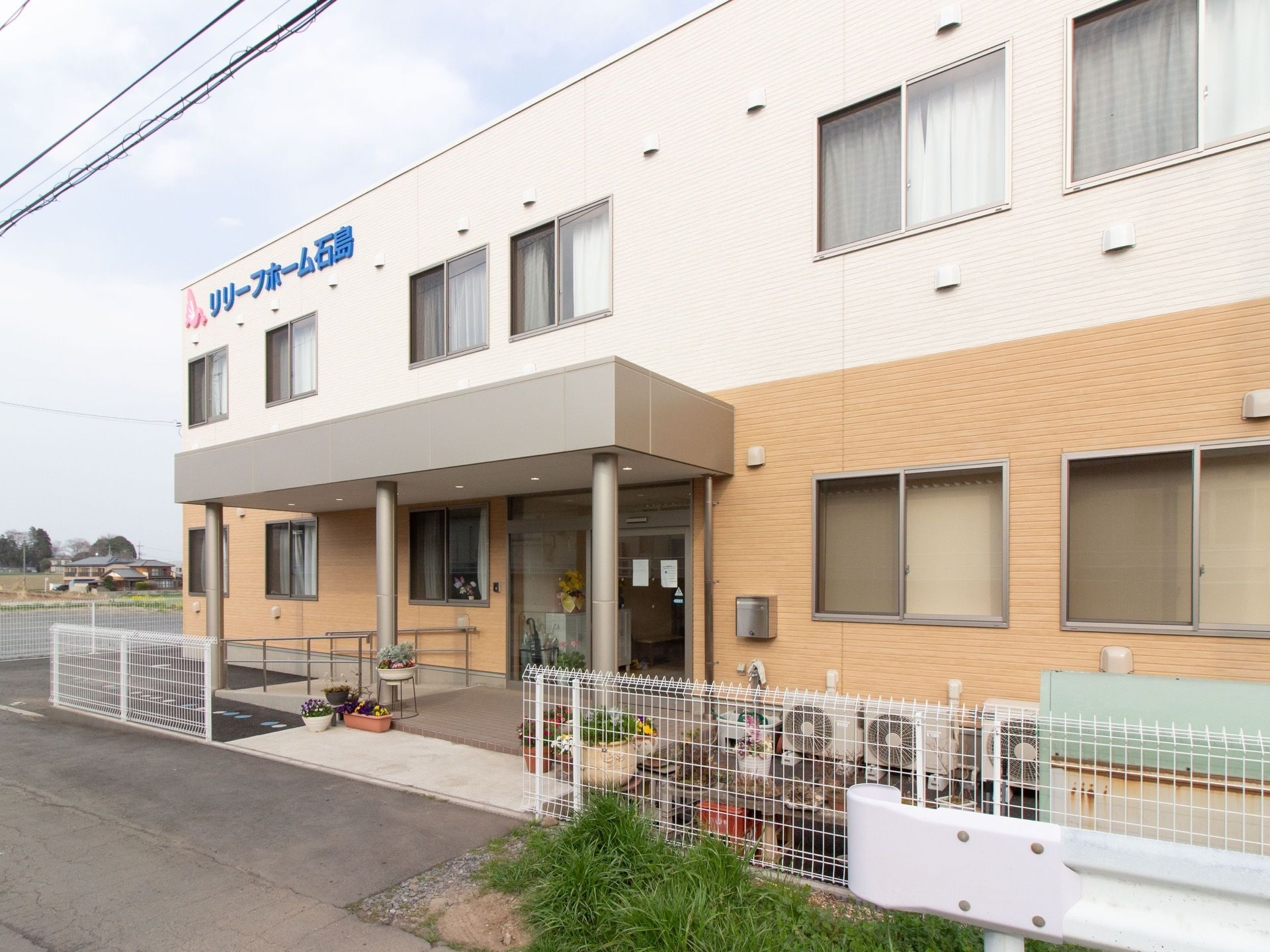 玄関前にひさしがついている。敷地境界には白い格子のフェンスが設置されている。玄関から道路までゆるやかなスロープになっている。