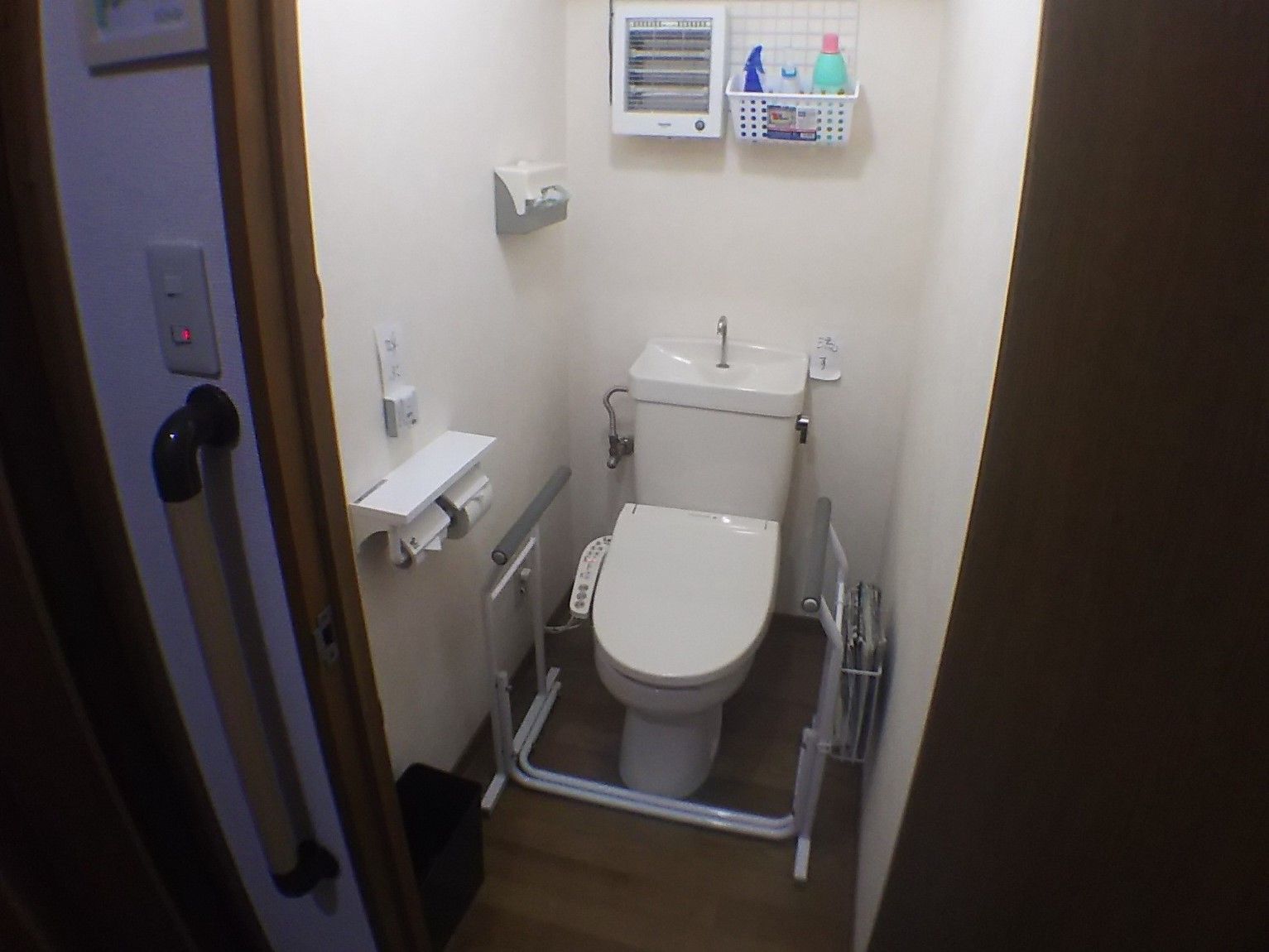 移動できる手すりを設置した居室内のトイレである。シャワー機能がついているので快適にお使いになれる。壁には緊急呼び出しボタンがある。