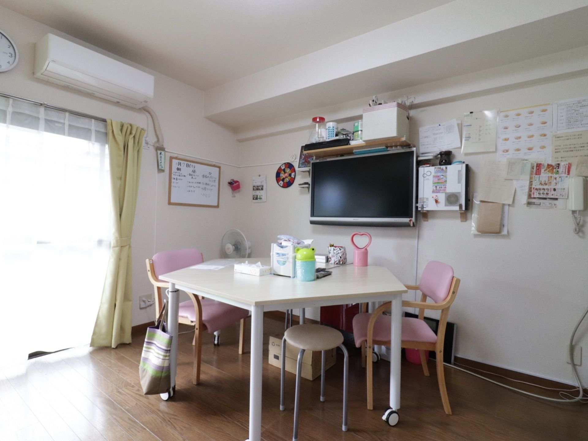 五角形のテーブルとピンクの椅子がある。壁にはホワイトボードやテレビが取り付けてあり、エアコンも完備されている。
