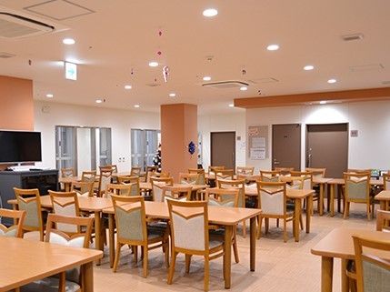 木製の椅子やテーブルがいくつも並ぶ広めのリビングスペース。施設内の共有スペースの写真