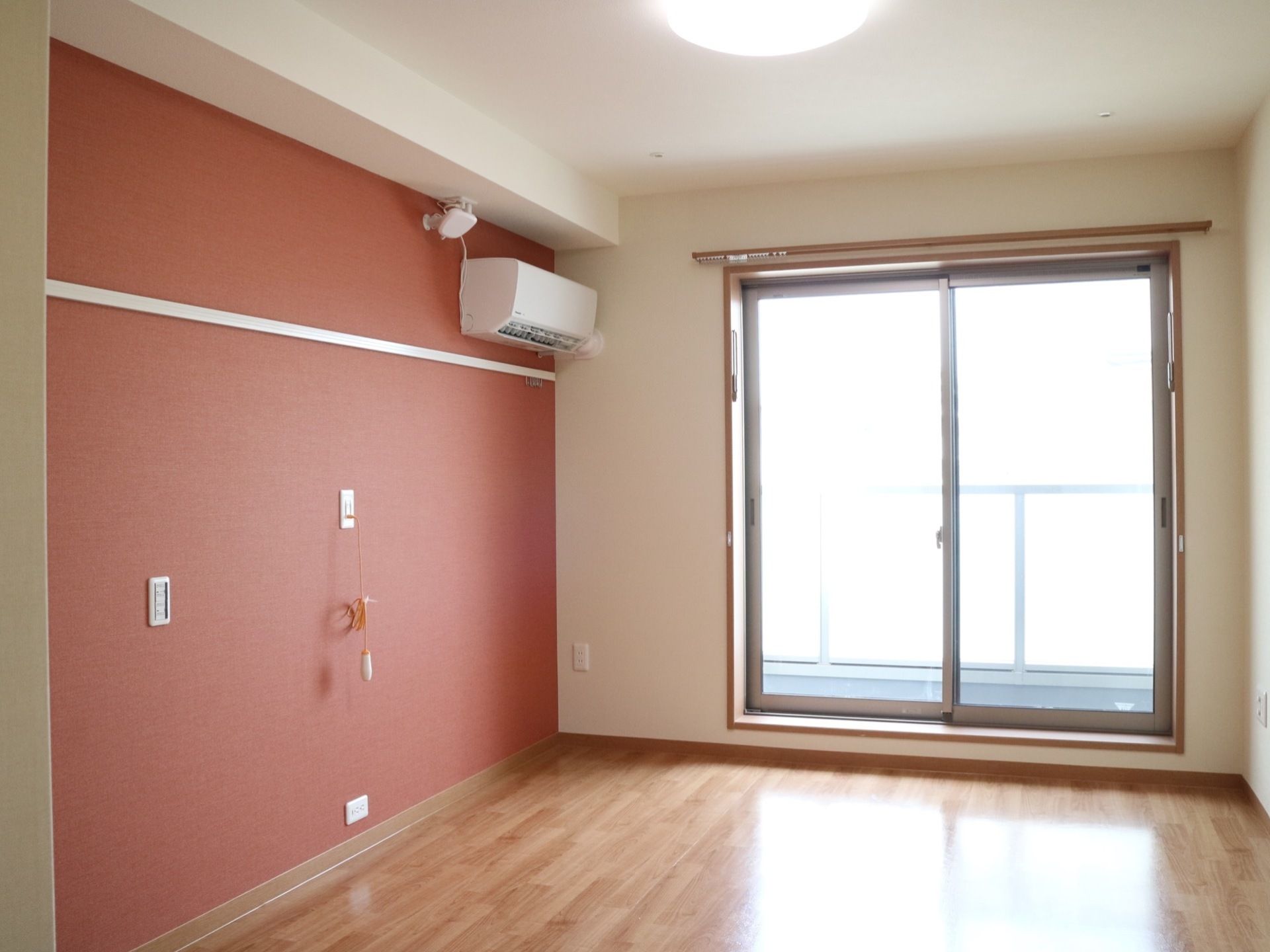 白を基調とした居室。壁の一部に落ち着いた赤茶色のアクセントクロスが使われている。モダンでおしゃれな雰囲気である。