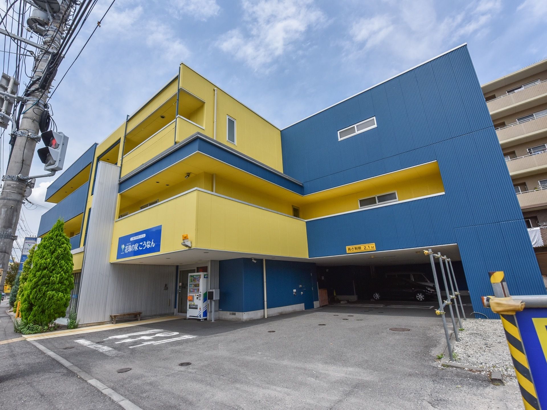 ブルーとイエローを組み合わせたデザインの外観で、３階建ての建物である。エントランスは広々としており、１階部分に駐車場が設けられている。