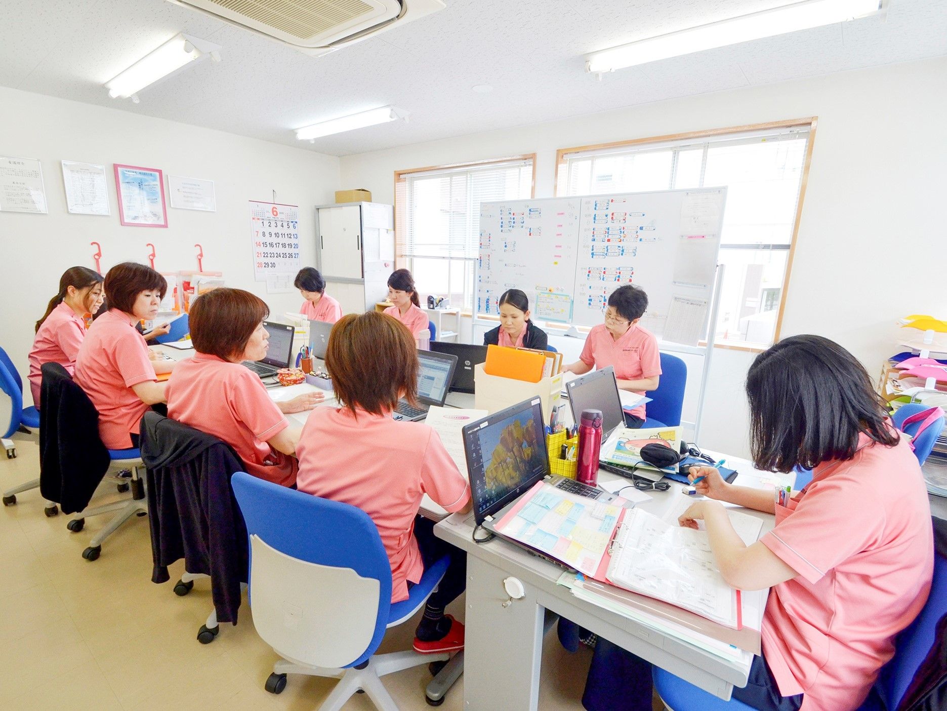 明るい事務室で、パソコンを前にして会議をするスタッフ