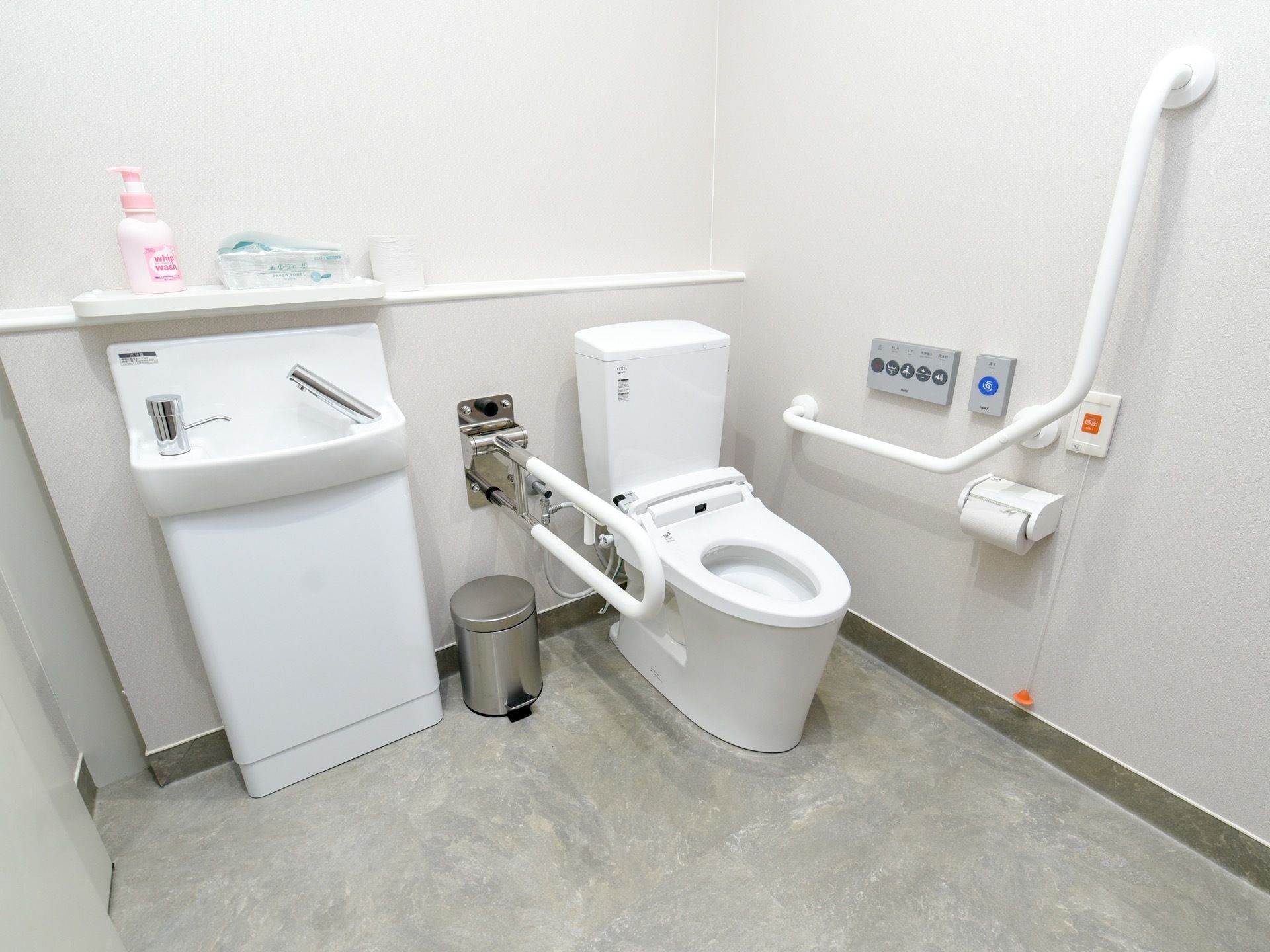 白い便器を設置した明るいトイレである。手すりを便器の両側に取りつけており、立ち座りの際に体を支えることができる。