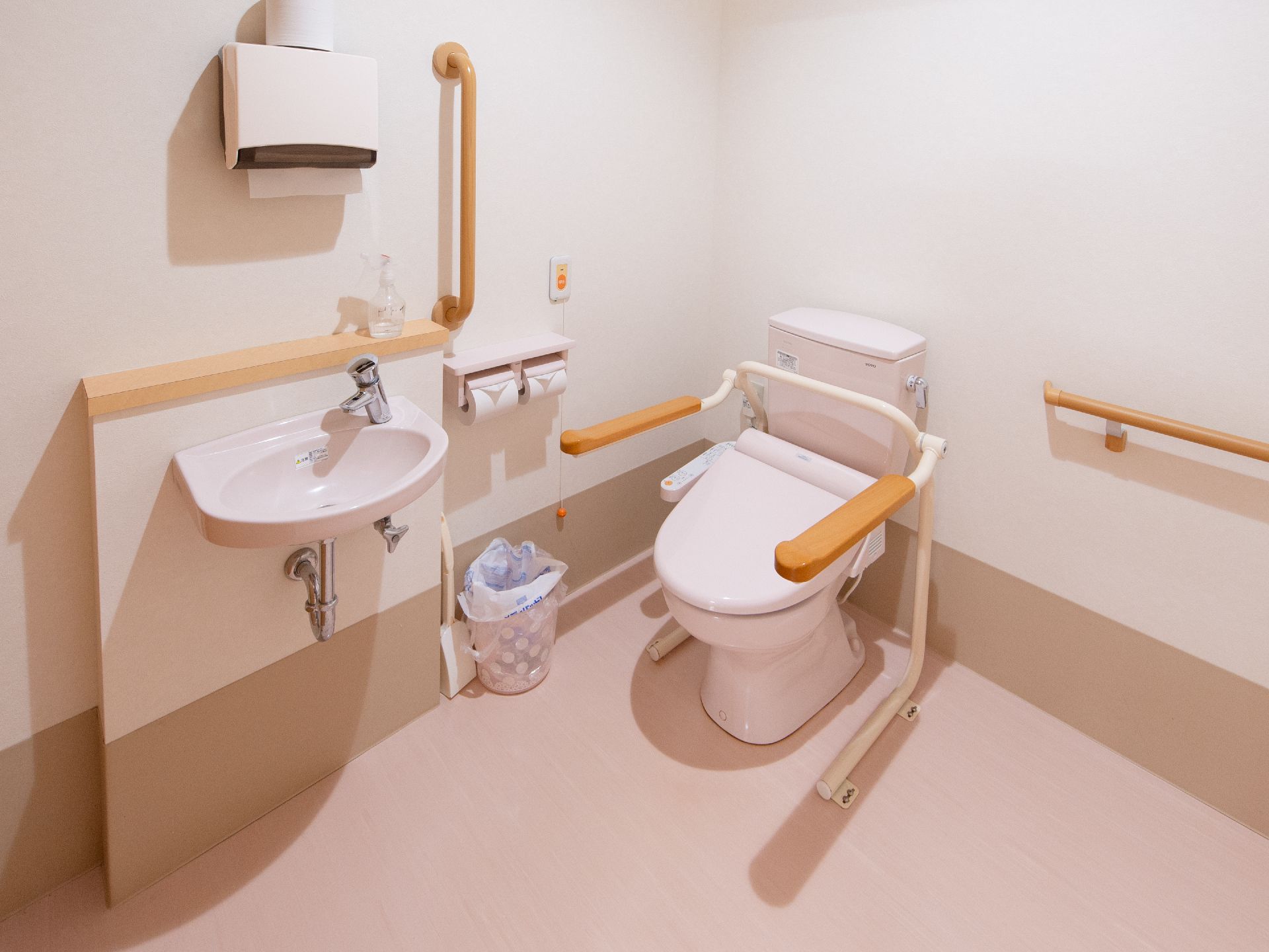 淡い配色のやさしい雰囲気のトイレには、温水洗浄便座が完備され、壁には手すりや緊急ブザーが設置されている。