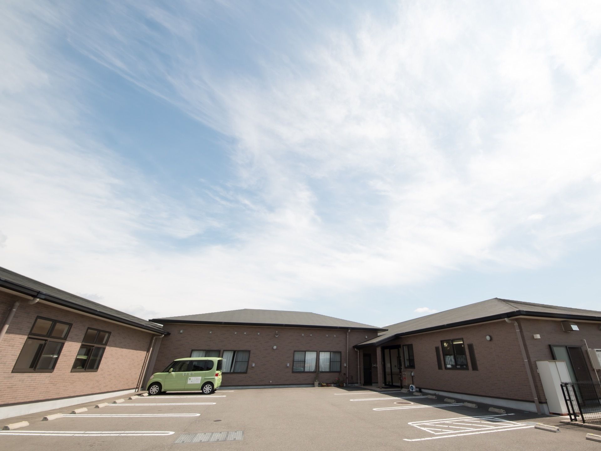 茶系の落ち着いた外壁の、コの字型の平屋造りの建物である。敷地内は舗装され、広い駐車場が整備されている。