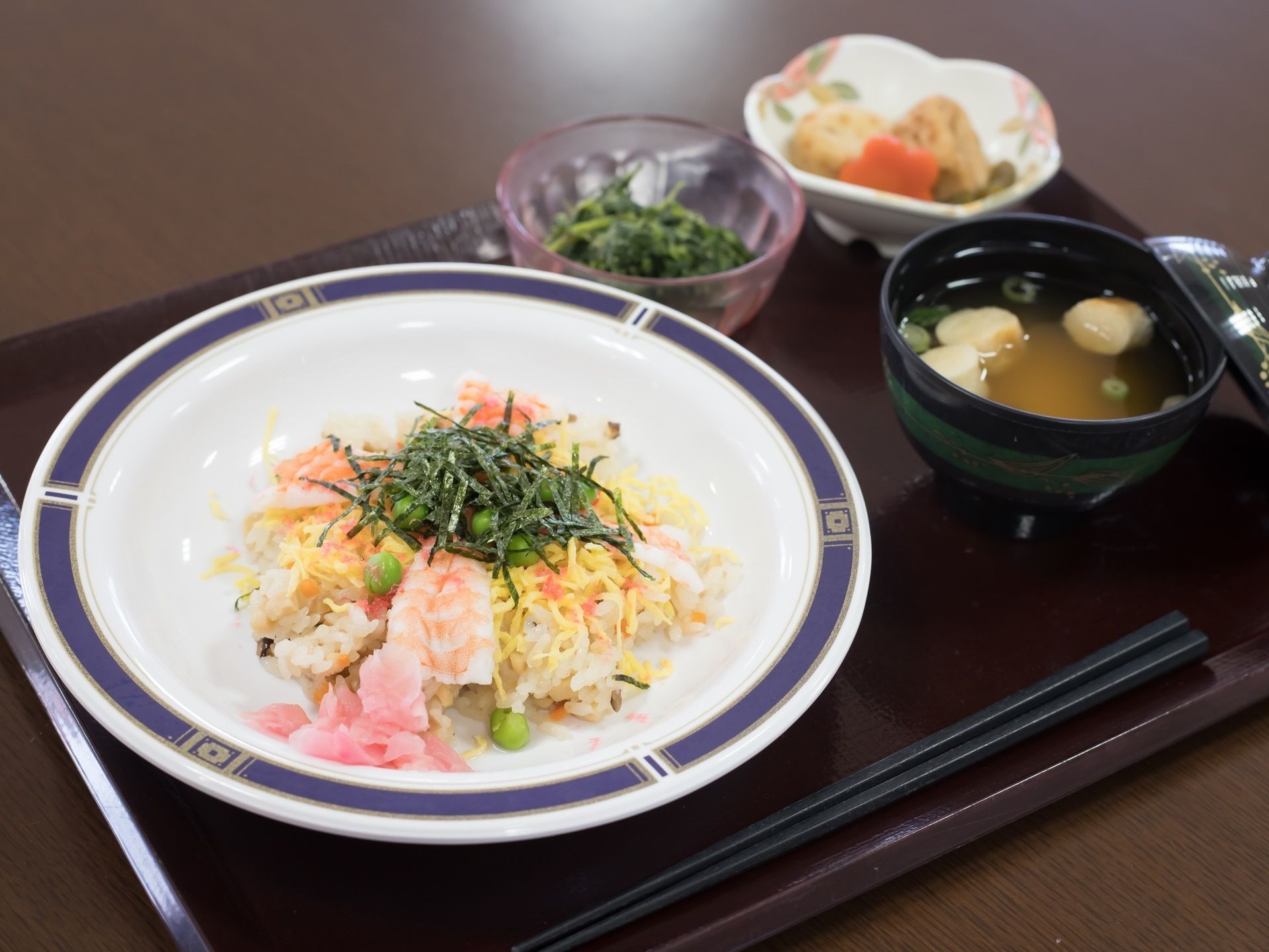 黒色のトレーの上に食事の支度がされている。ちらし寿司とすまし汁、煮物、青菜のおひたしのメニューである。