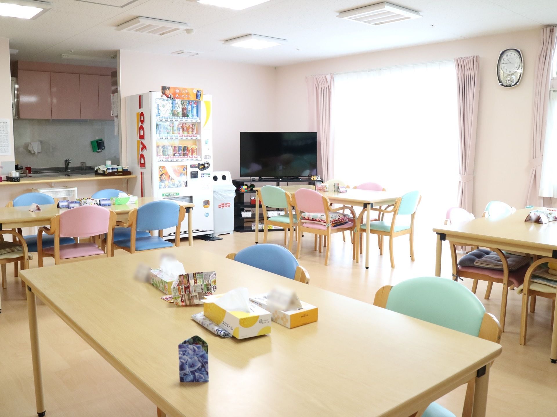 テーブルが並ぶ共有スペースである。室内にはテレビや自動販売機が備わっており、対面式のキッチンが併設されている。