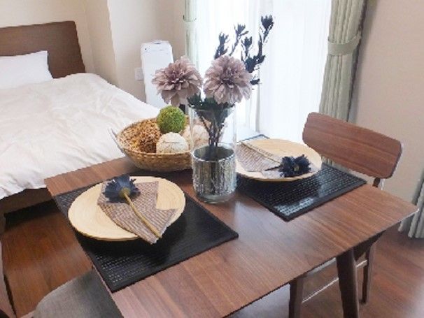 木製のテーブルとイスが置かれた部屋。奥には白いシーツがかかったベッドが置かれている。