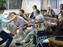 椅子に座っている大勢の入居者と一緒に手の体操をしているスタッフ