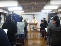 十字架が掲げられている前に神父の男性がおり、その話を聞いている入居者様