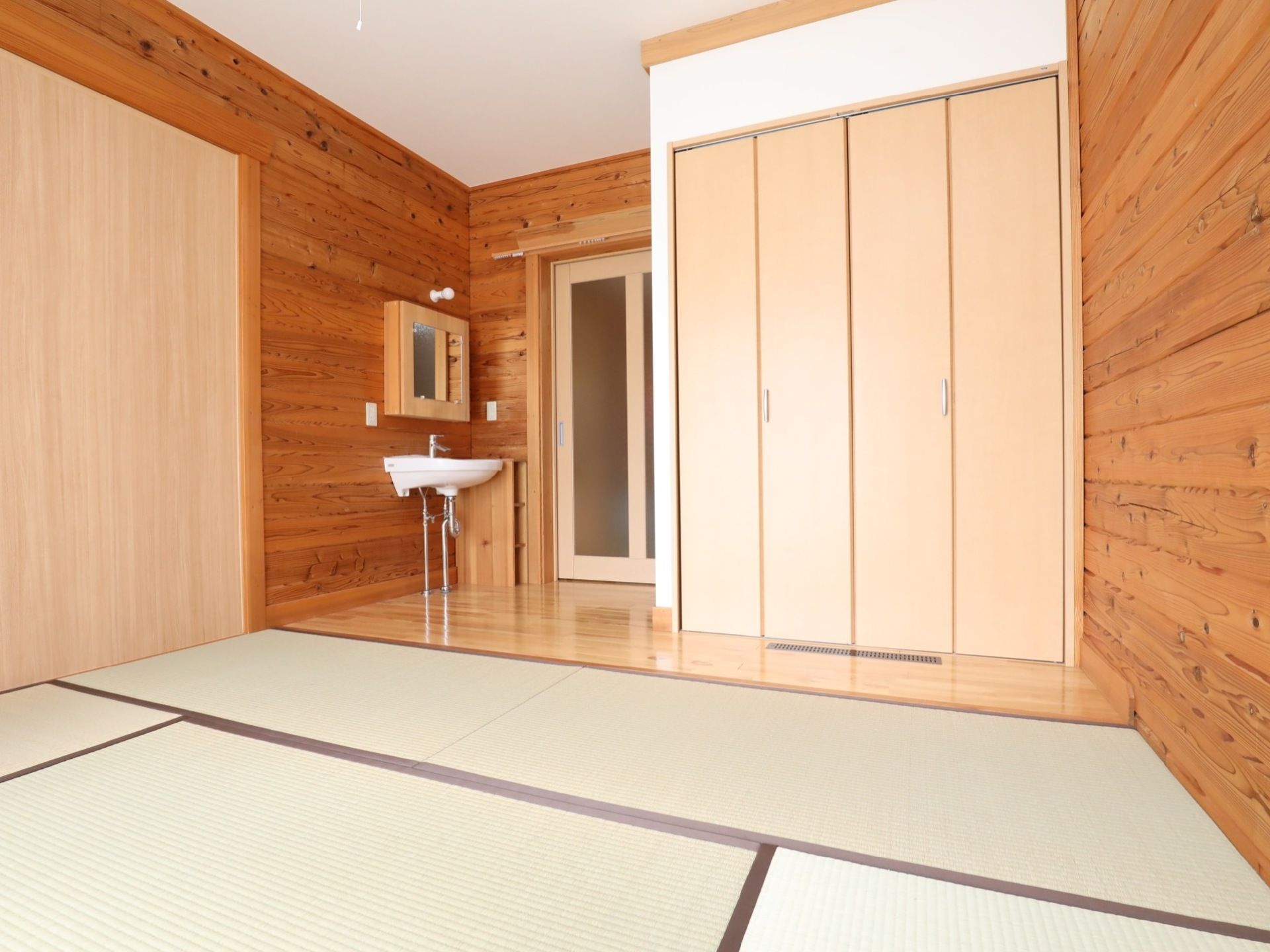 居室には、すりガラスの入った出入口の扉や背の高い開き戸タイプの収納がある。部屋の奥の方には広い畳のスペースがある。