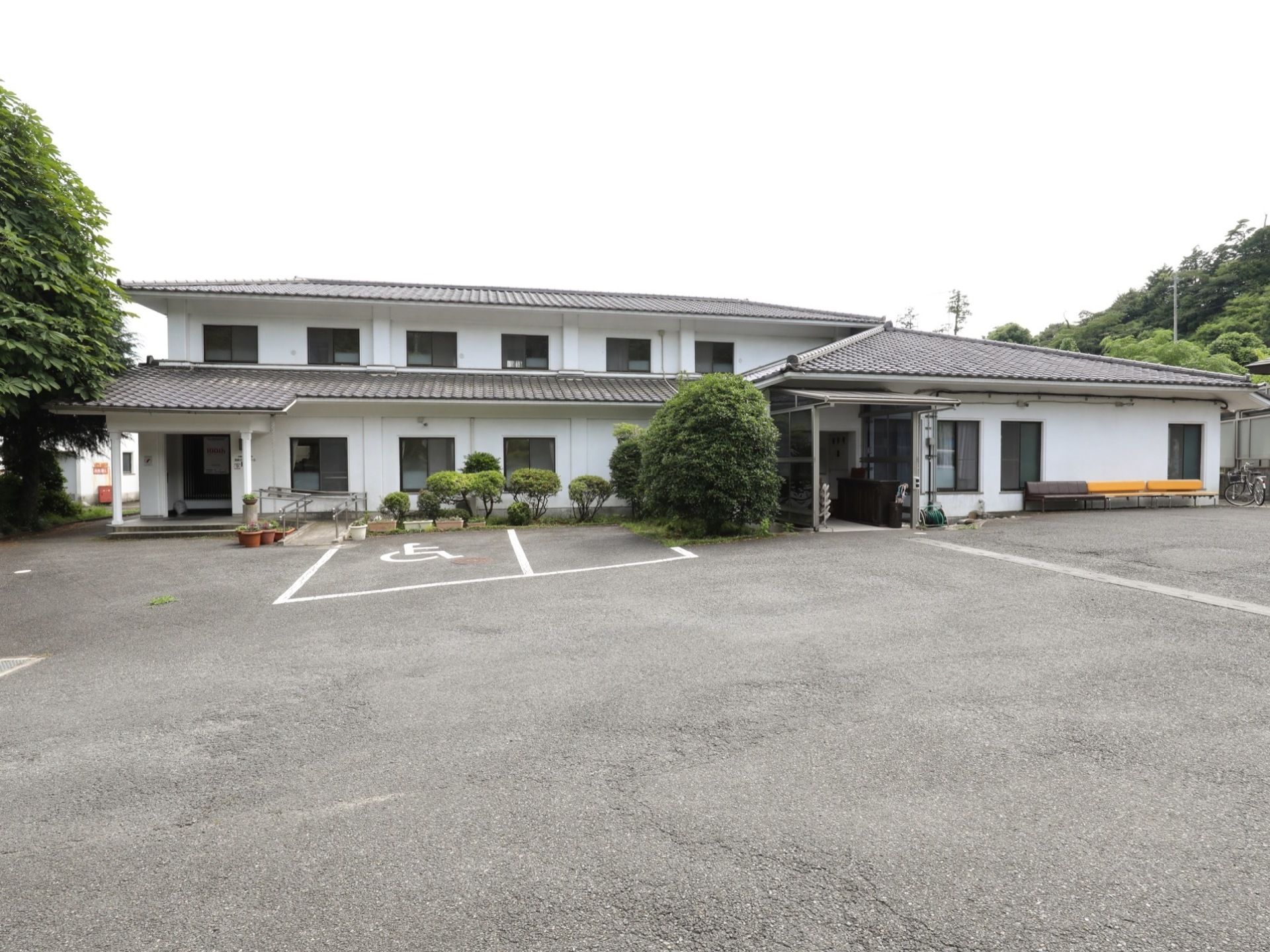 白色の壁と瓦屋根の建物になっている。広い敷地に立地しており、車椅子をご利用の方用の駐車スペースが確保されている。