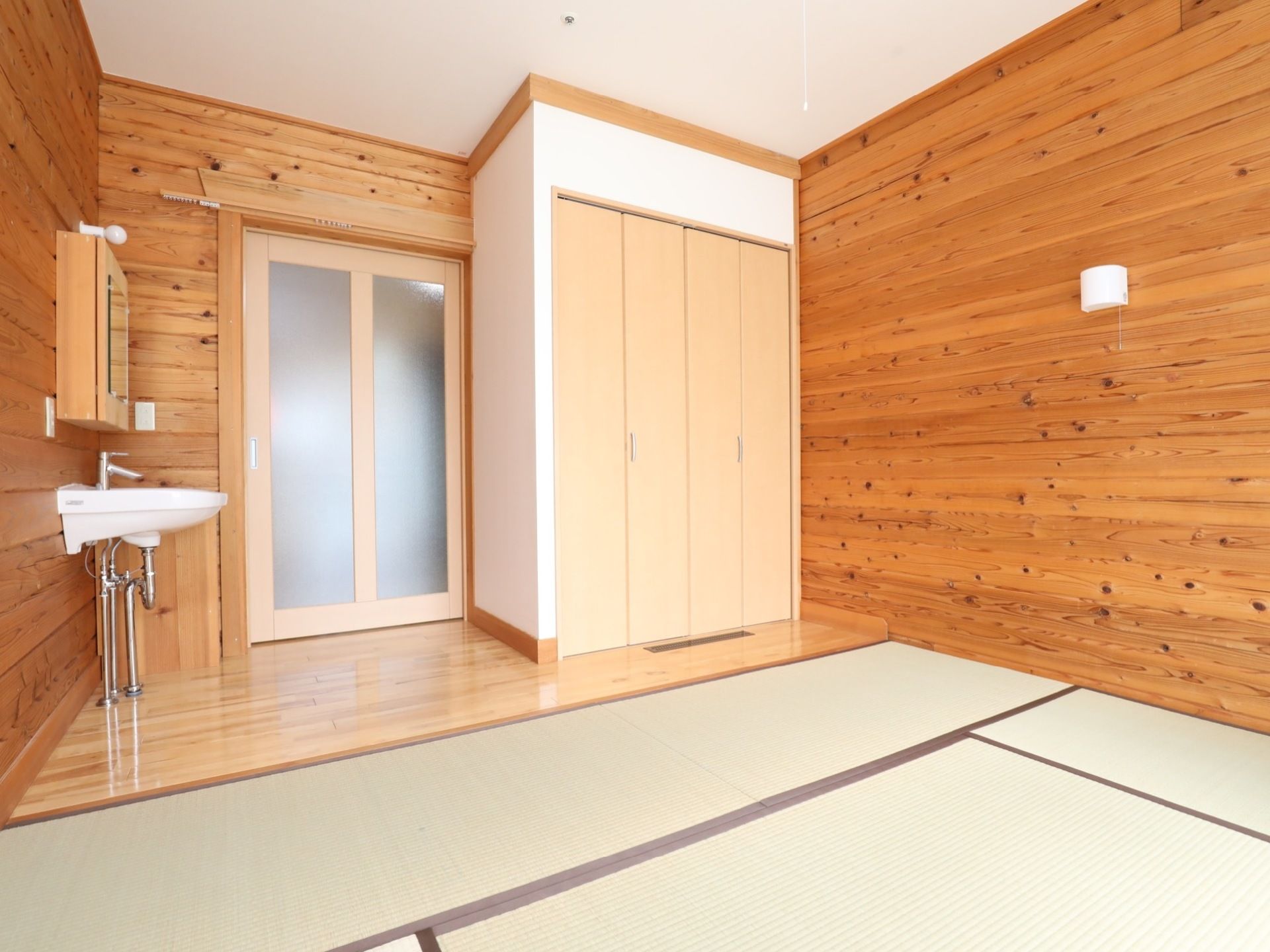 木材を使った壁に畳が敷かれた部屋。大きな引き戸の入り口を入って右手に洗面台、左手にクローゼットがある。