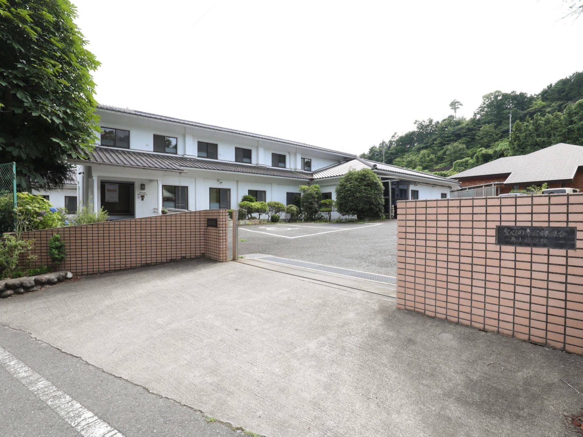 車がすれ違える幅がある門の中にある敷地に、白い壁で２階建の建物がある。建物の前には駐車スペースが設けられている。