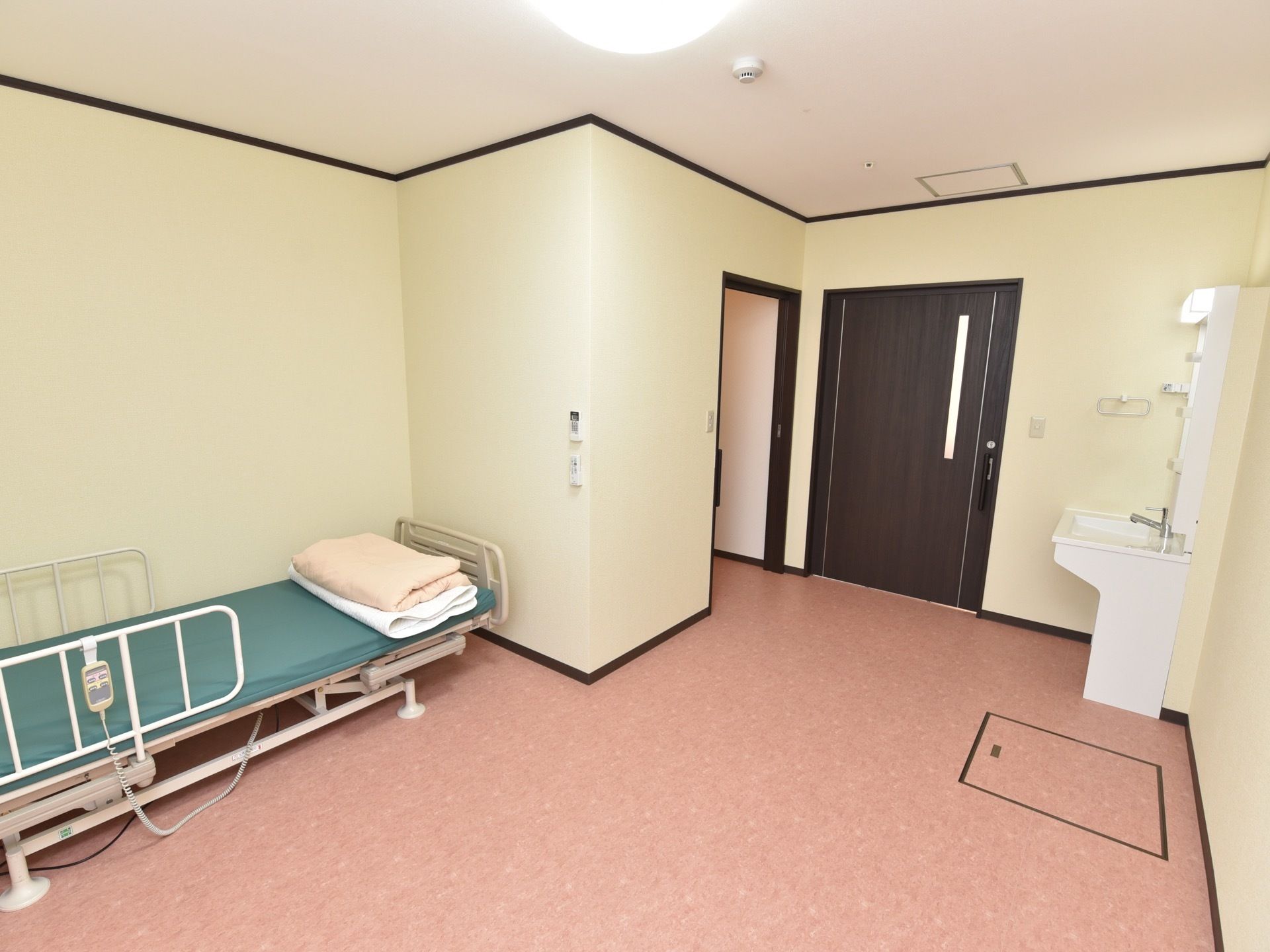 クリーム色の壁にピンク色の床の内装である。リモコンが掛けられた柵がついたベッドが置いてあり、入口の付近に洗面台が設置されている。